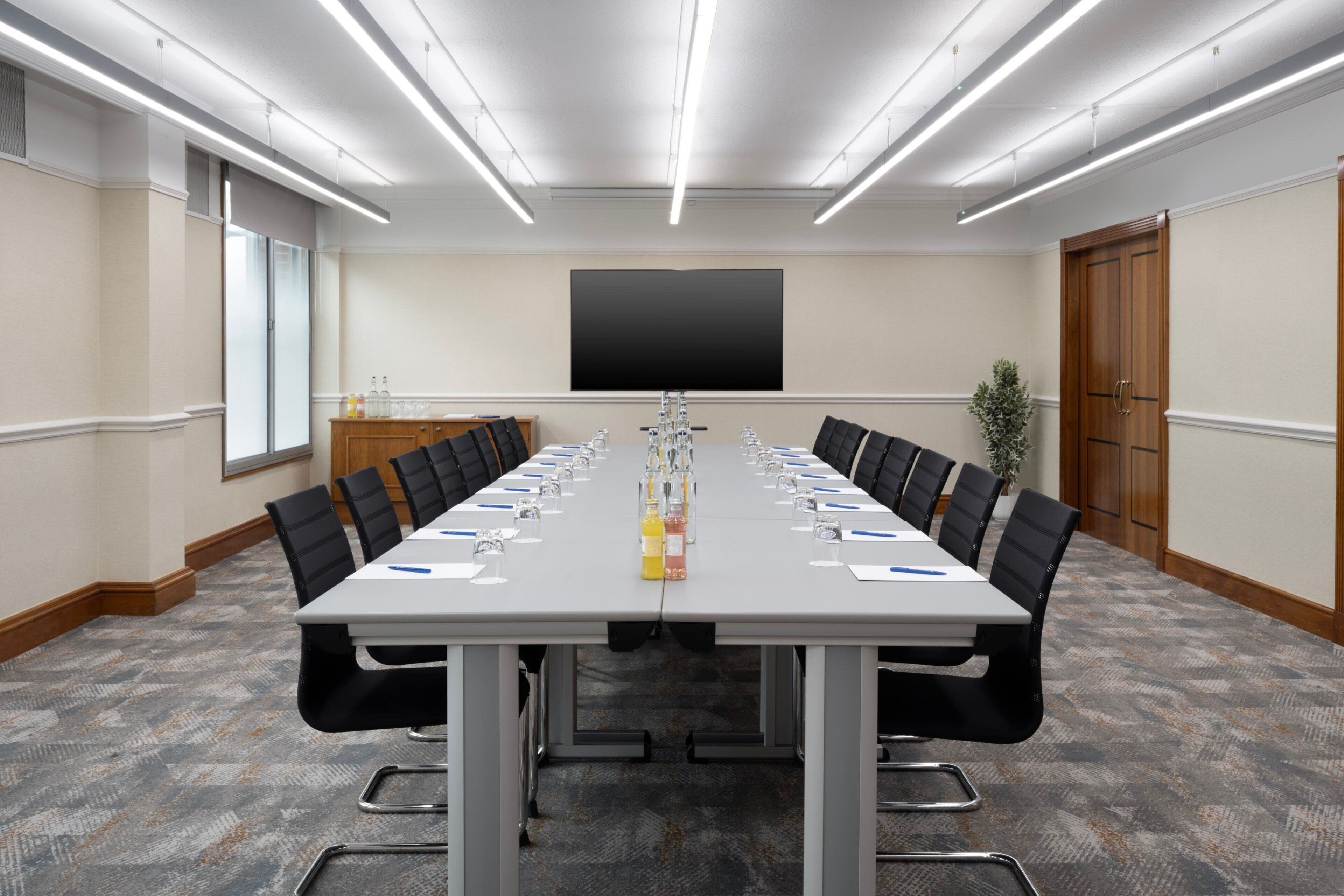 A conference room with a long table, chairs, a projector screen, and a plant.