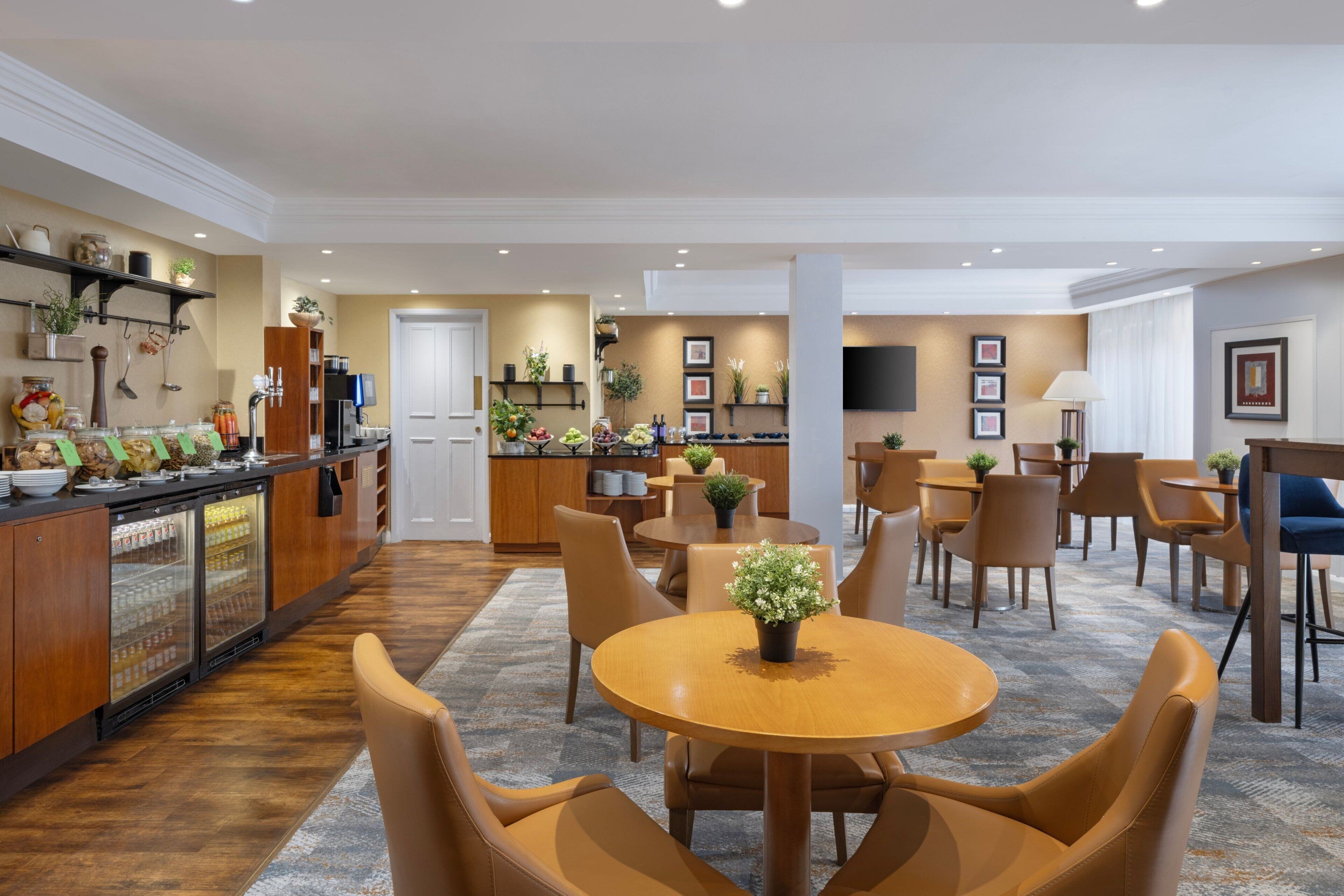 A modern hotel lobby with a bar area, seating arrangements, and a kitchen in the background.