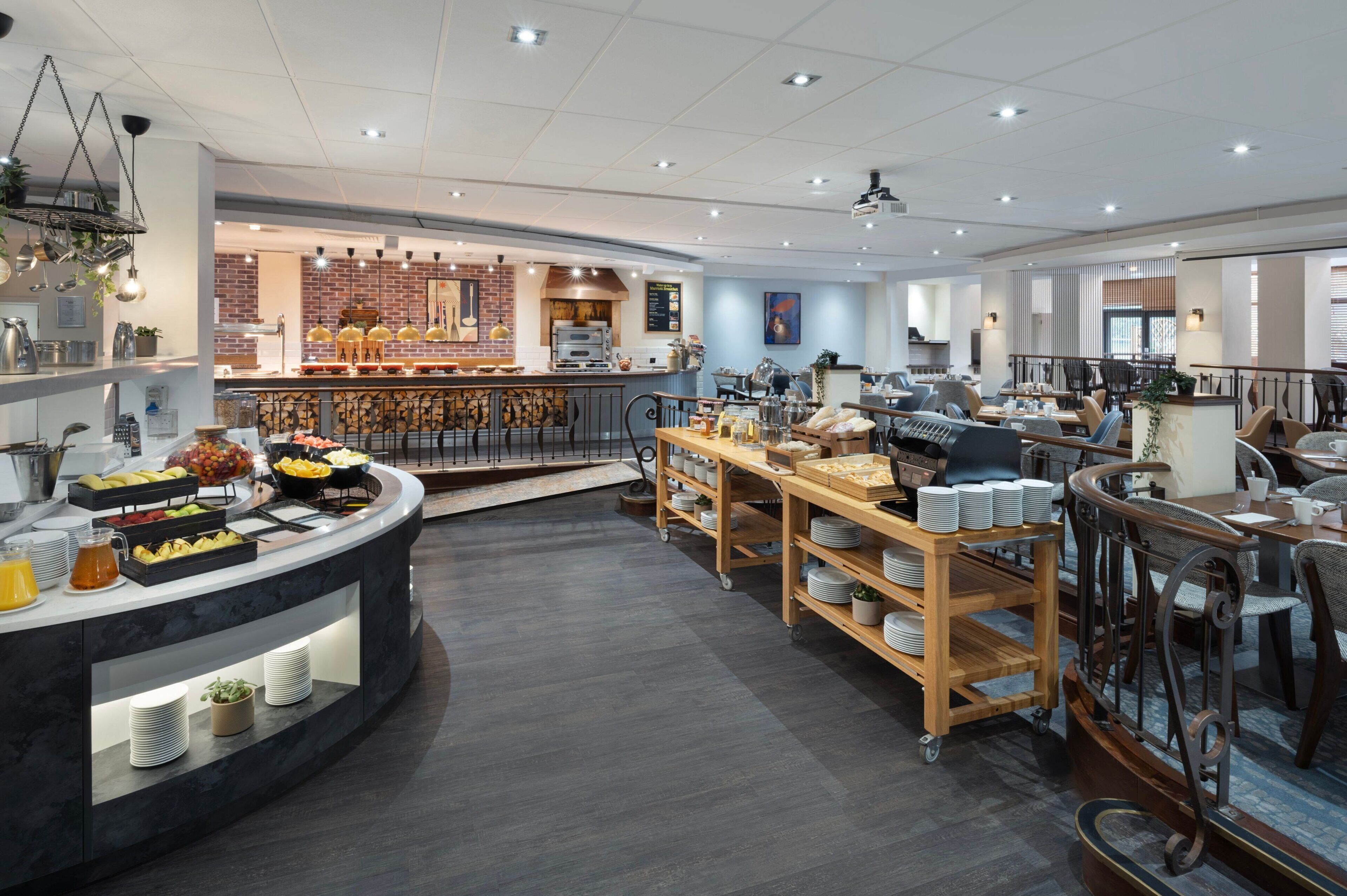 Un restaurante moderno con una barra central, una zona de buffet con diversas opciones de comida y diferentes disposiciones de mesas.