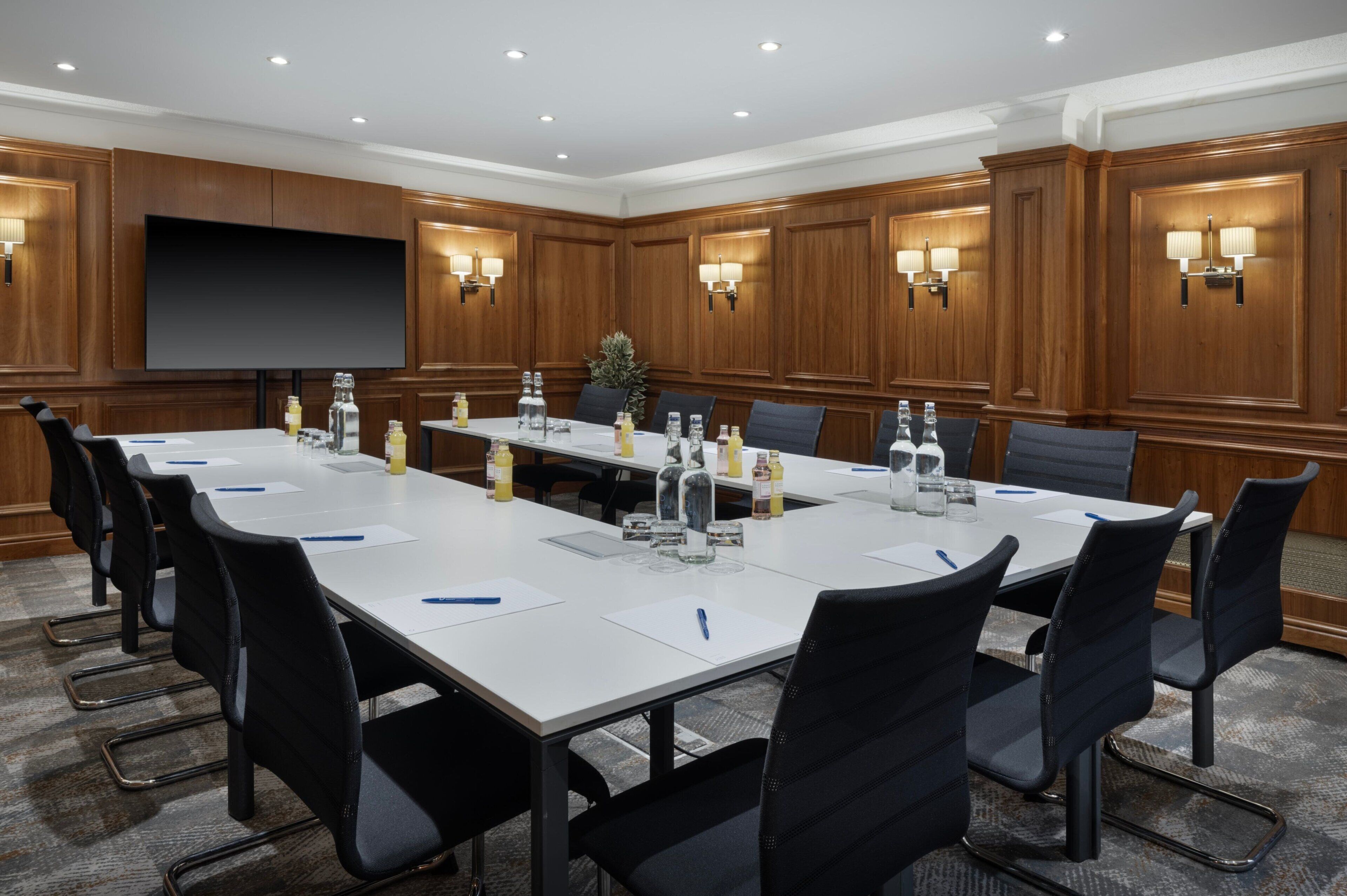 A conference room with a long table, black chairs, a large screen, and wall-mounted lamps.