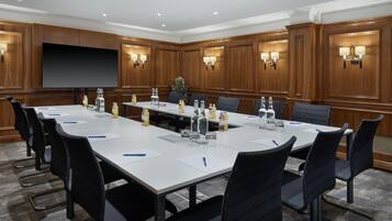 A conference room with a long table, black chairs, a large screen, and wall-mounted lamps.