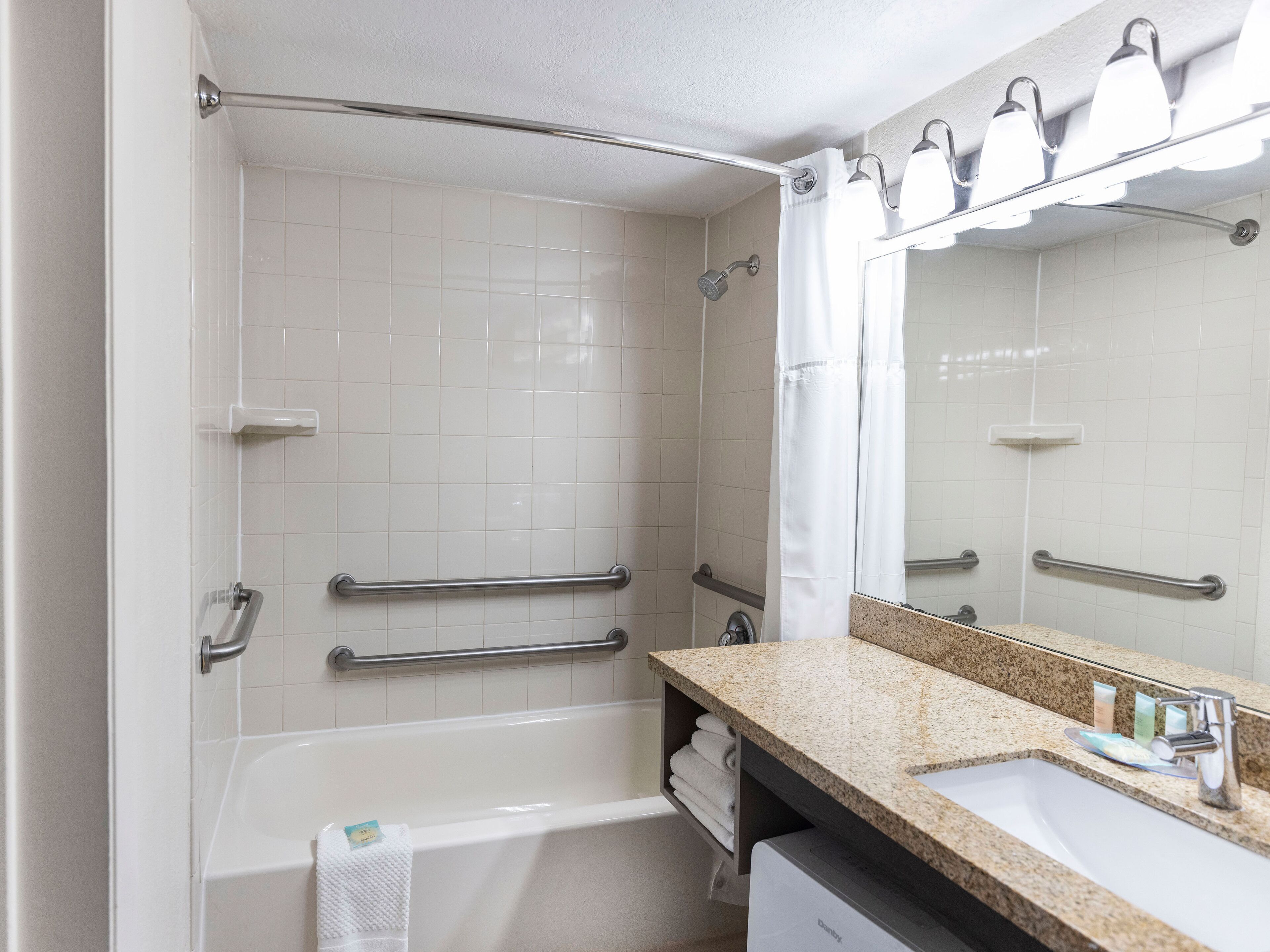 A modern bathroom with a bathtub, a vanity with a sink, and a mirror. There are grab bars in the shower area.