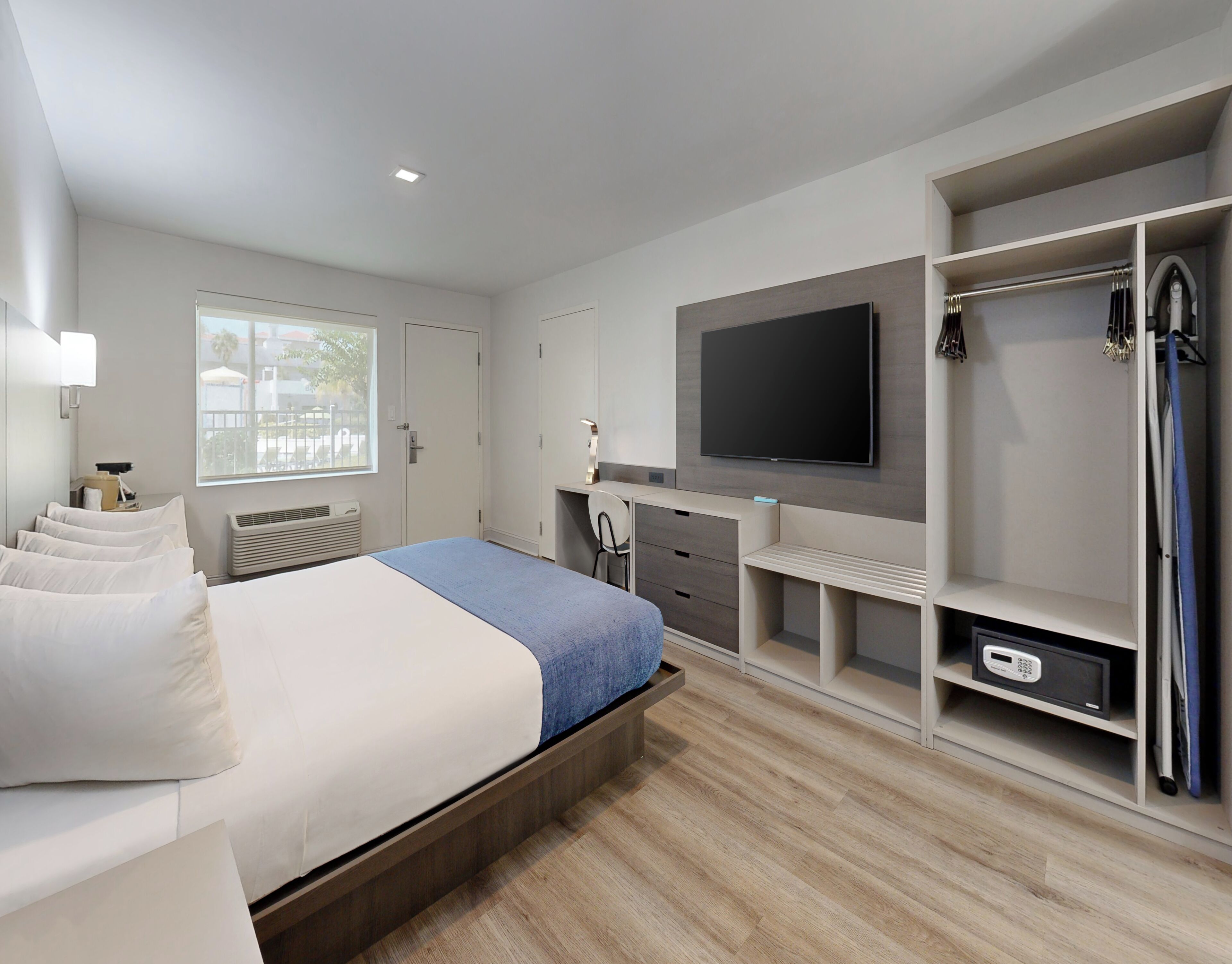 Una habitación de hotel moderna con cama, escritorio, televisor y vestidor.