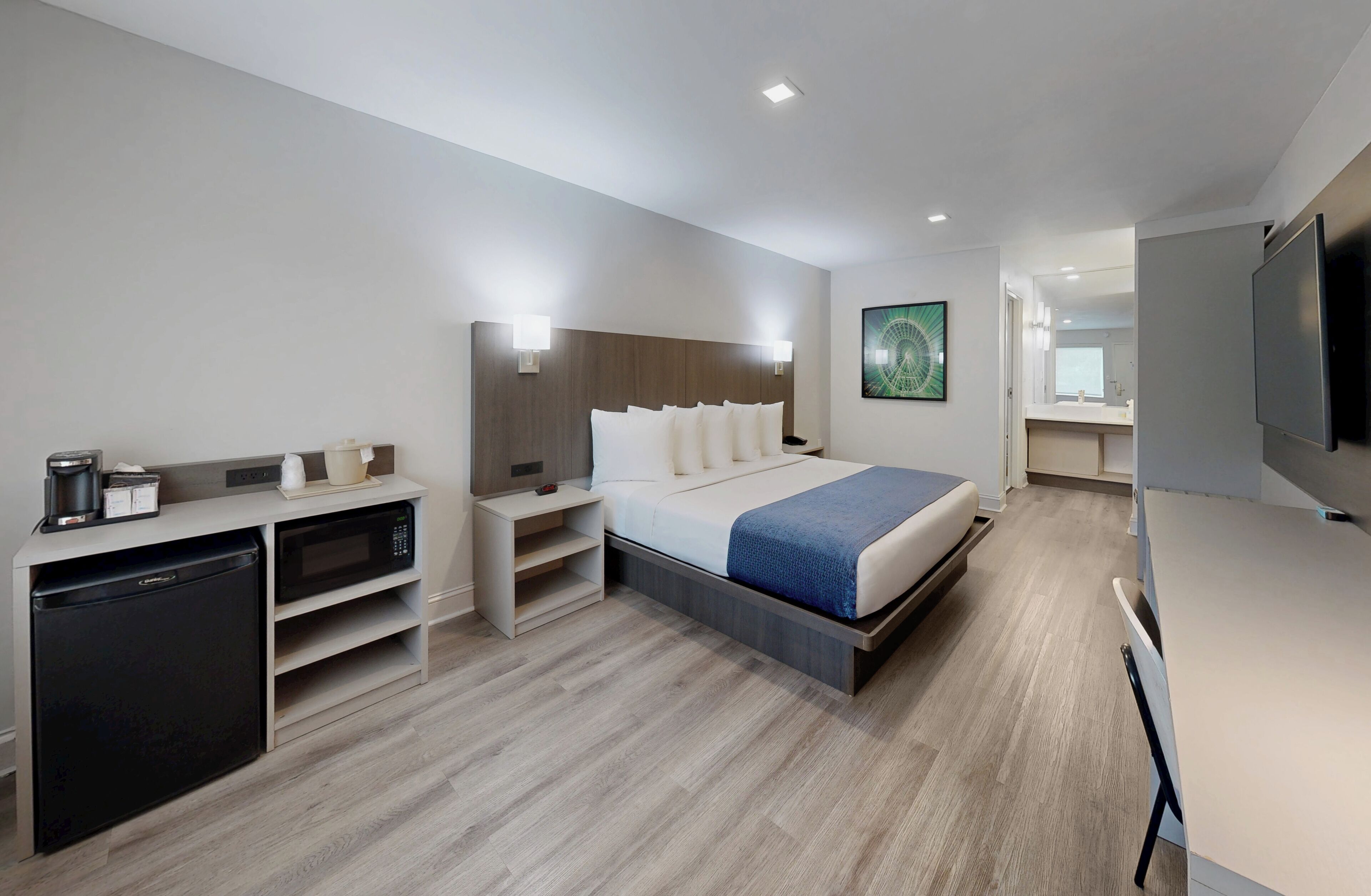 A modern hotel room with a bed, bedside tables, a built-in TV, a microwave, and a mini-fridge.