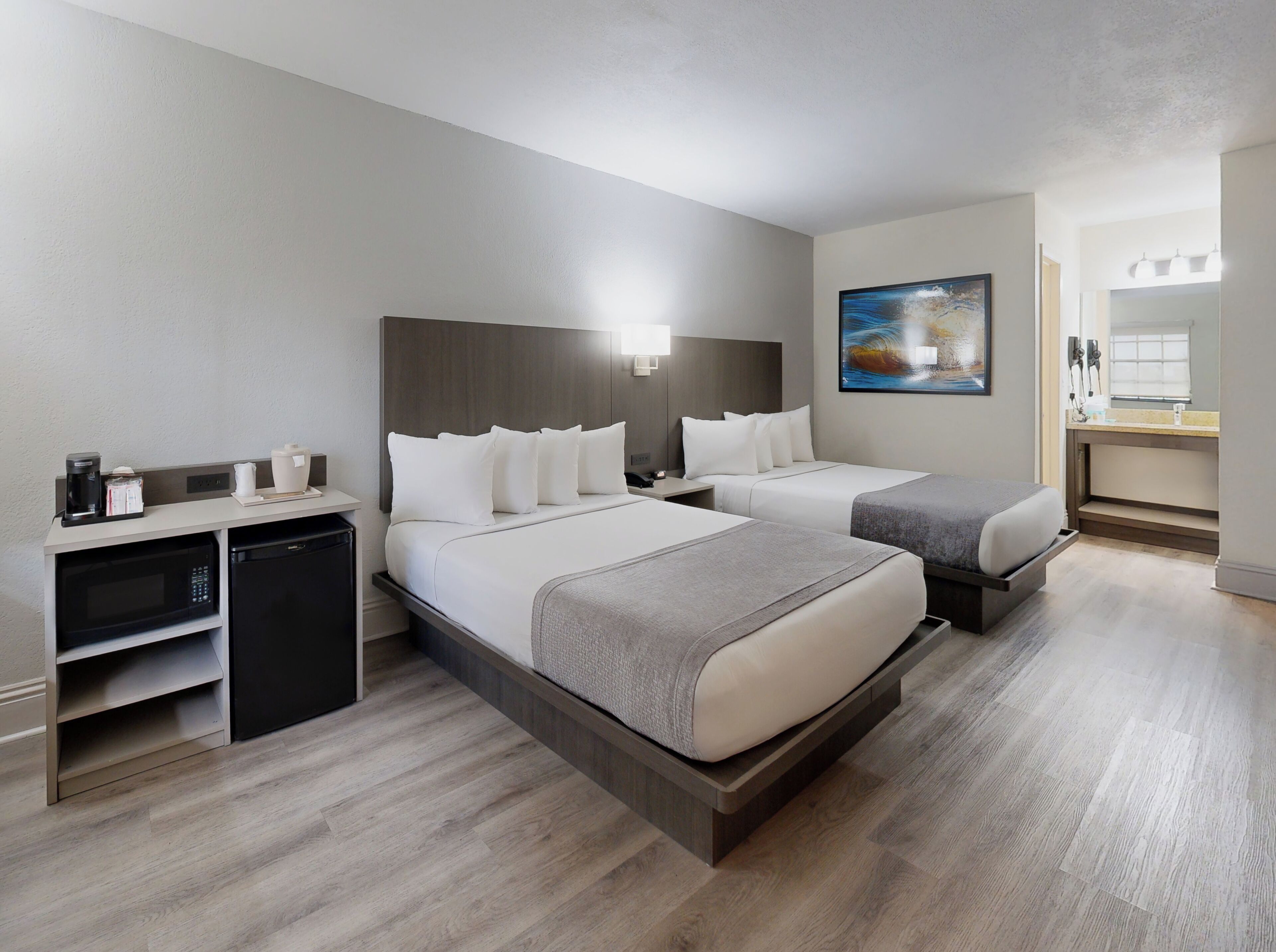 Habitación de hotel con dos camas, un escritorio, cafetera, microondas y un refrigerador pequeño.