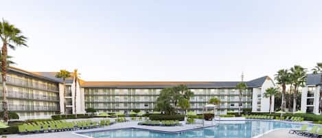 Un hotel con piscina, varios balcones y palmeras.