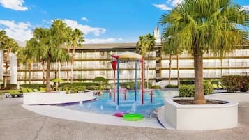 Relax by the pool surrounded by palm trees and lounge chairs, with a water play area and shaded seating.