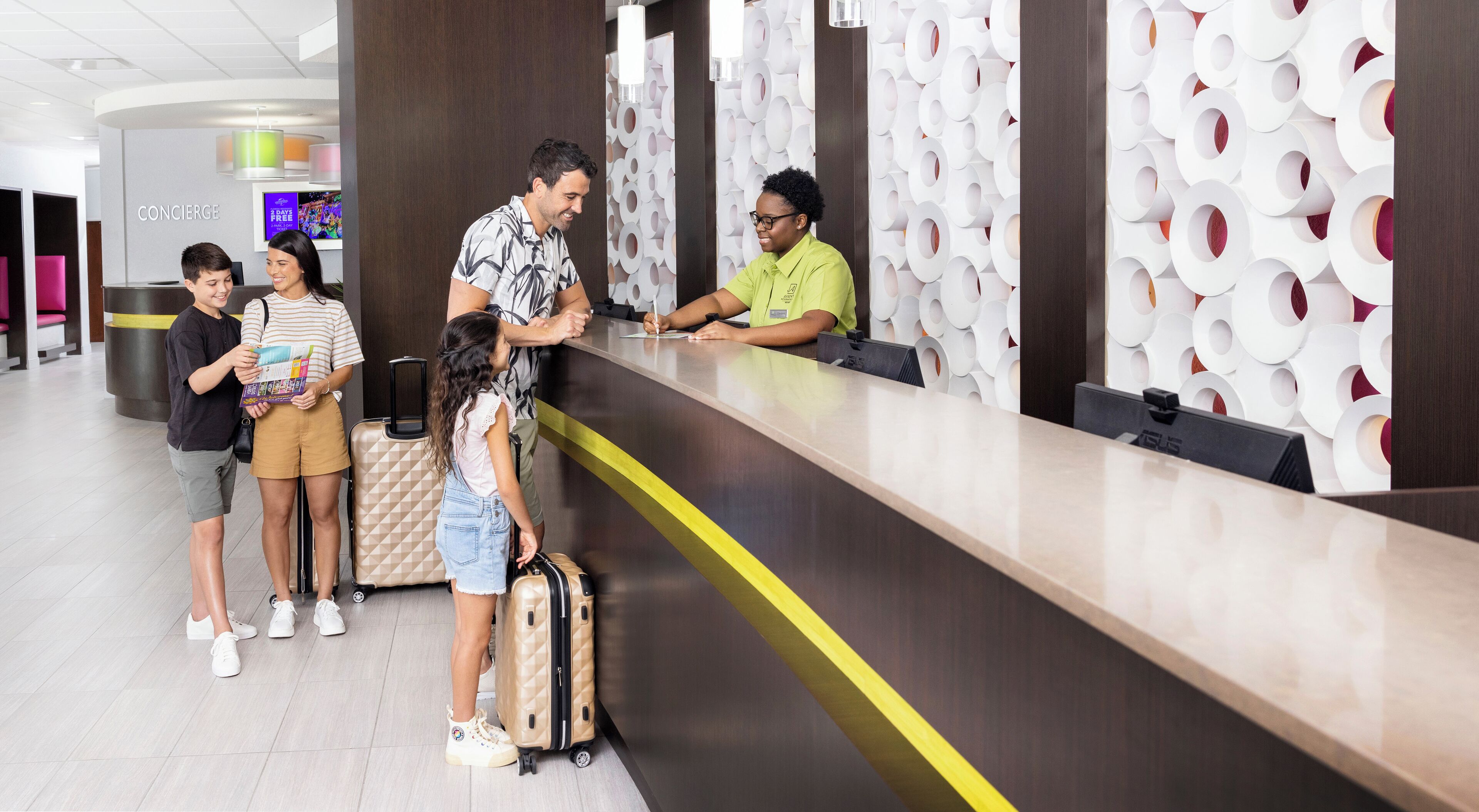 A hotel reception area with a modern design, including a reception desk, a concierge desk, and a wall with circular patterns. There are several guests standing and interacting with the staff.