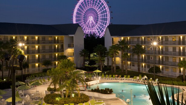 A hotel with a large Ferris wheel, a swimming pool, and multiple balconies. - Avanti International Resort (Orlando)