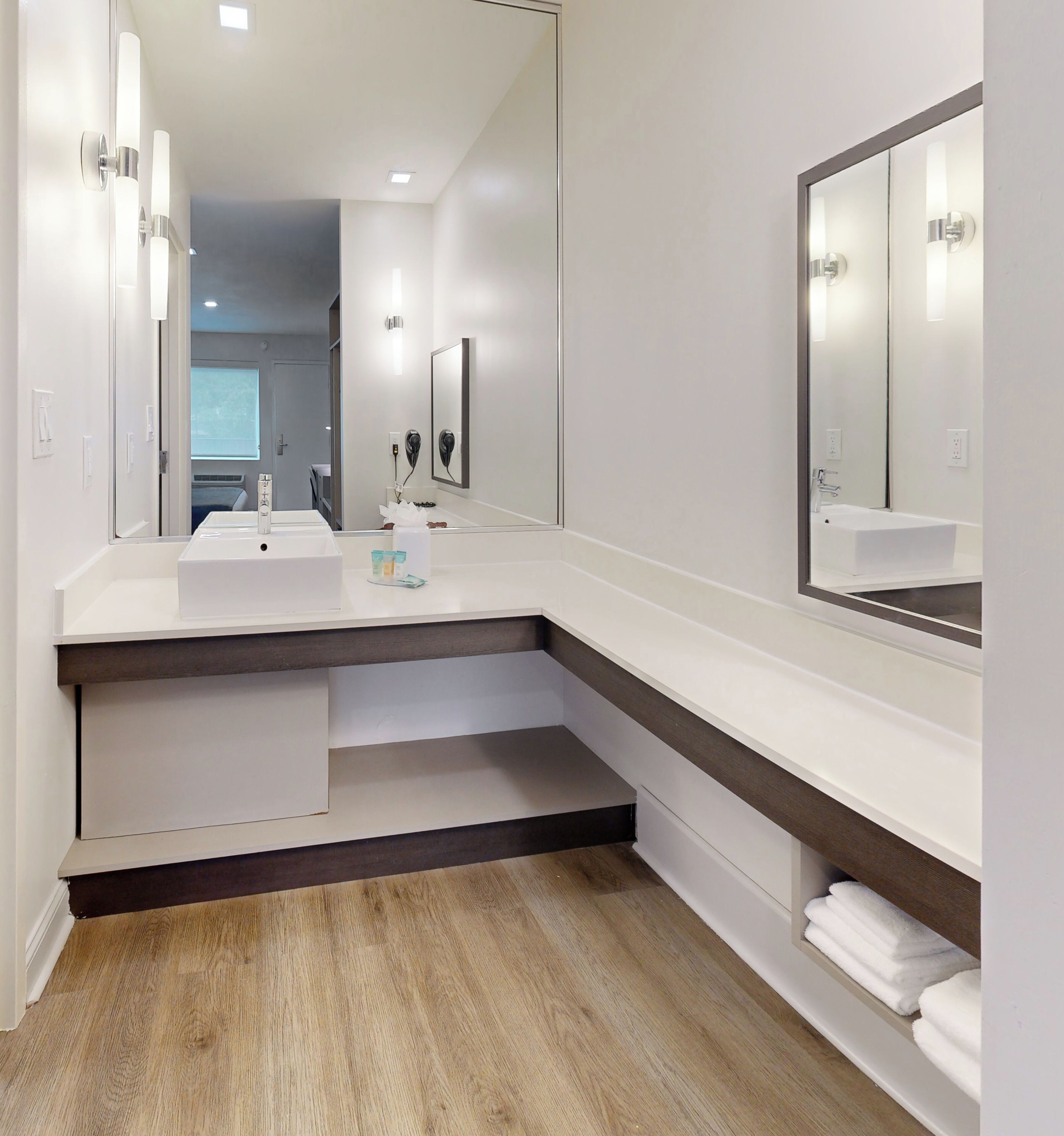 A modern bathroom with two sinks, a large mirror, and a wooden floor.