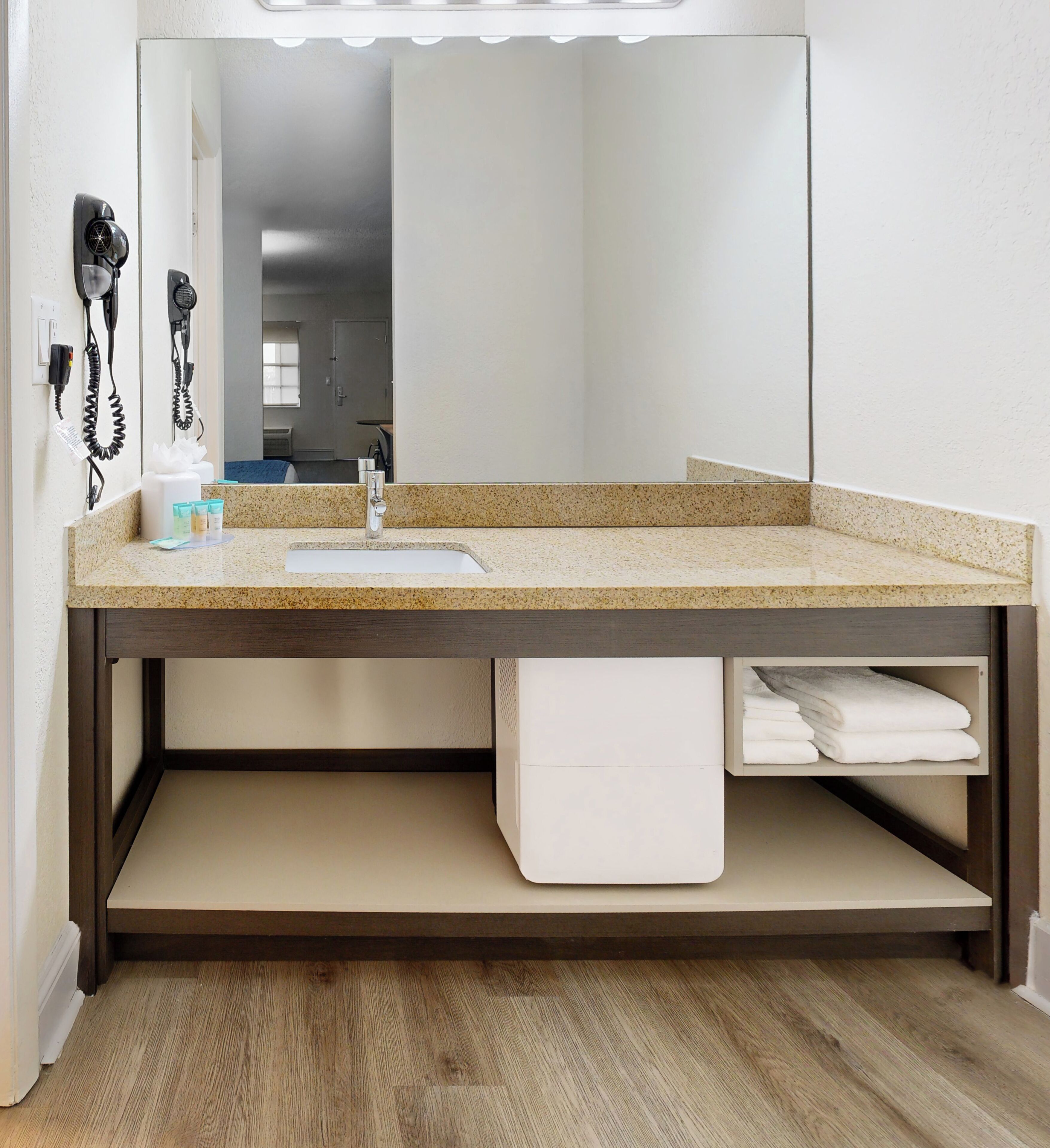 Un baño con encimera de granito, lavamanos, espejo y toallero.