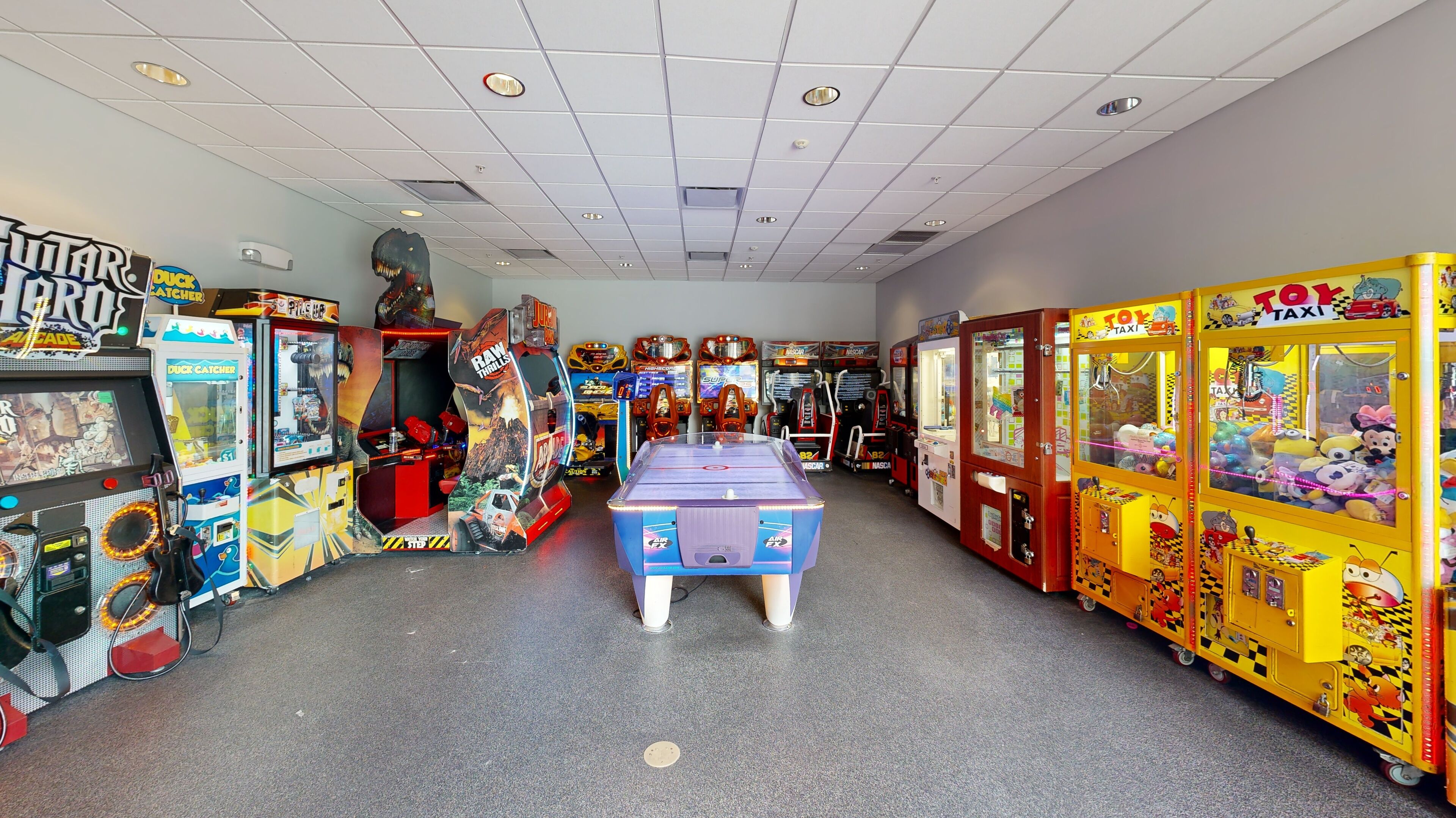 A room filled with various arcade games, including a pool table in the center.