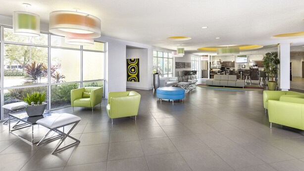 A spacious lobby with modern furniture, large windows, and a visible kitchen area. - Avanti International Resort (Orlando)