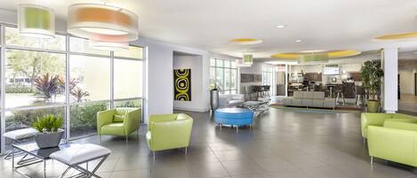 A spacious lobby with modern furniture, large windows, and a visible kitchen area.