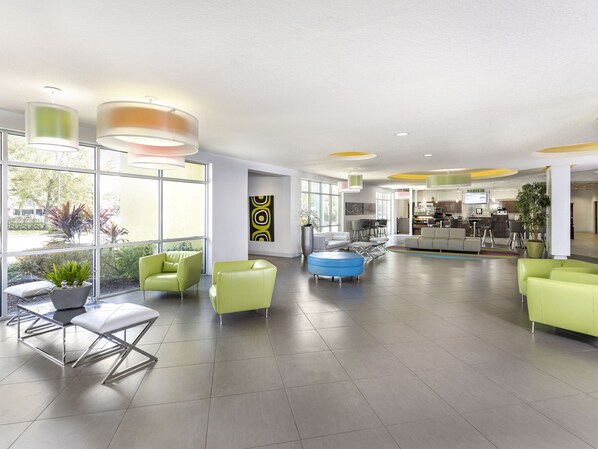 A spacious lobby with modern furniture, large windows, and a visible kitchen area. - Avanti International Resort (Orlando)
