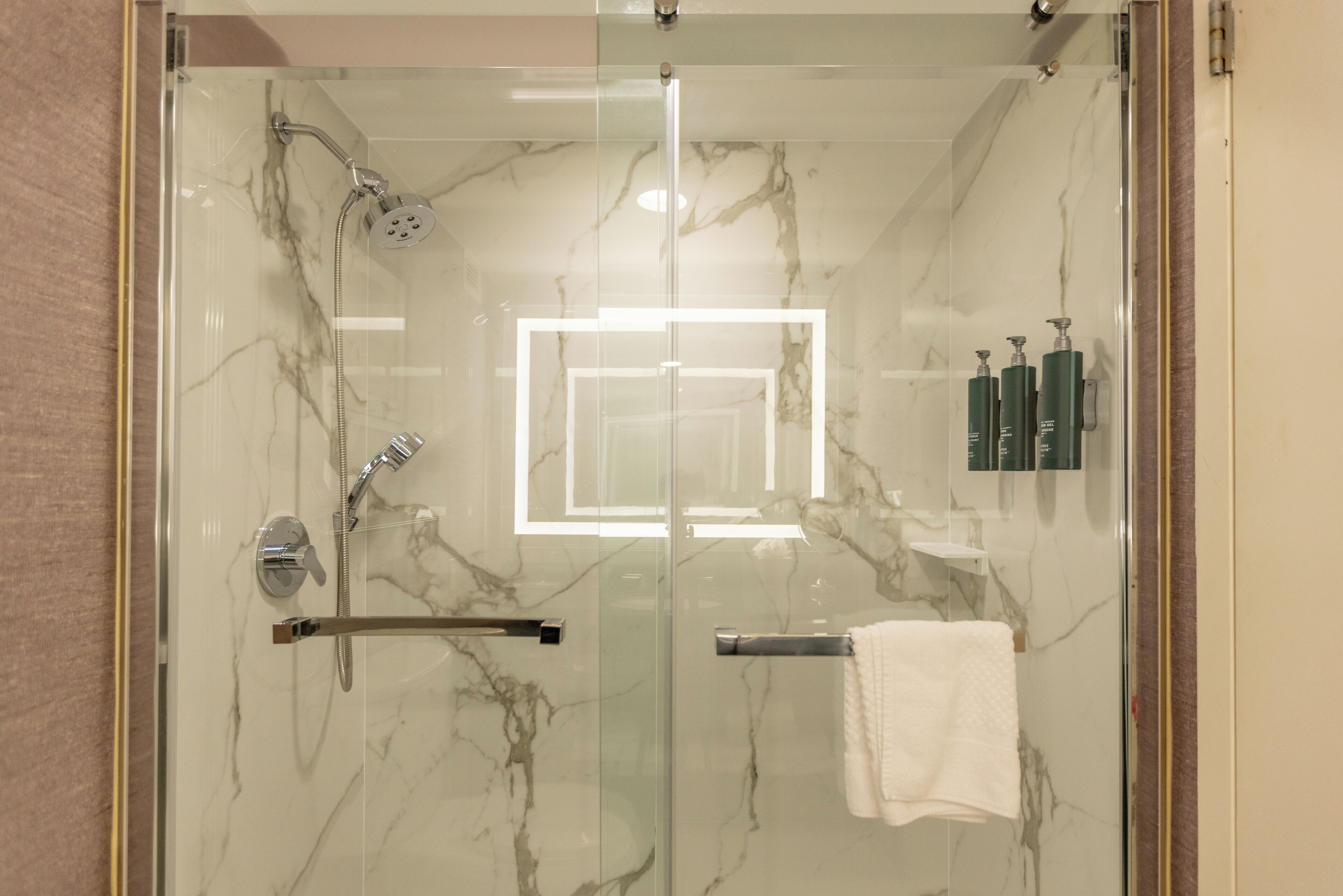 A modern bathroom with a glass-enclosed shower, marble walls, and a towel rack.