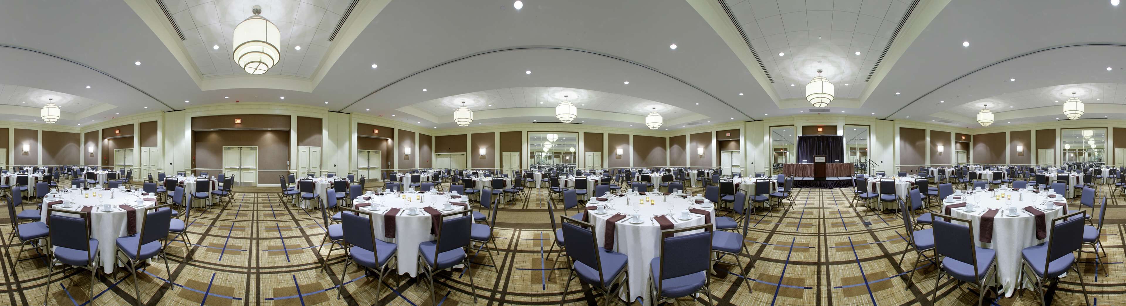 A large banquet hall with multiple round tables and chairs, equipped with white tablecloths and silverware.