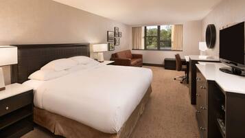 A hotel room with a large bed, a desk, a chair, a TV, and a window with curtains.
