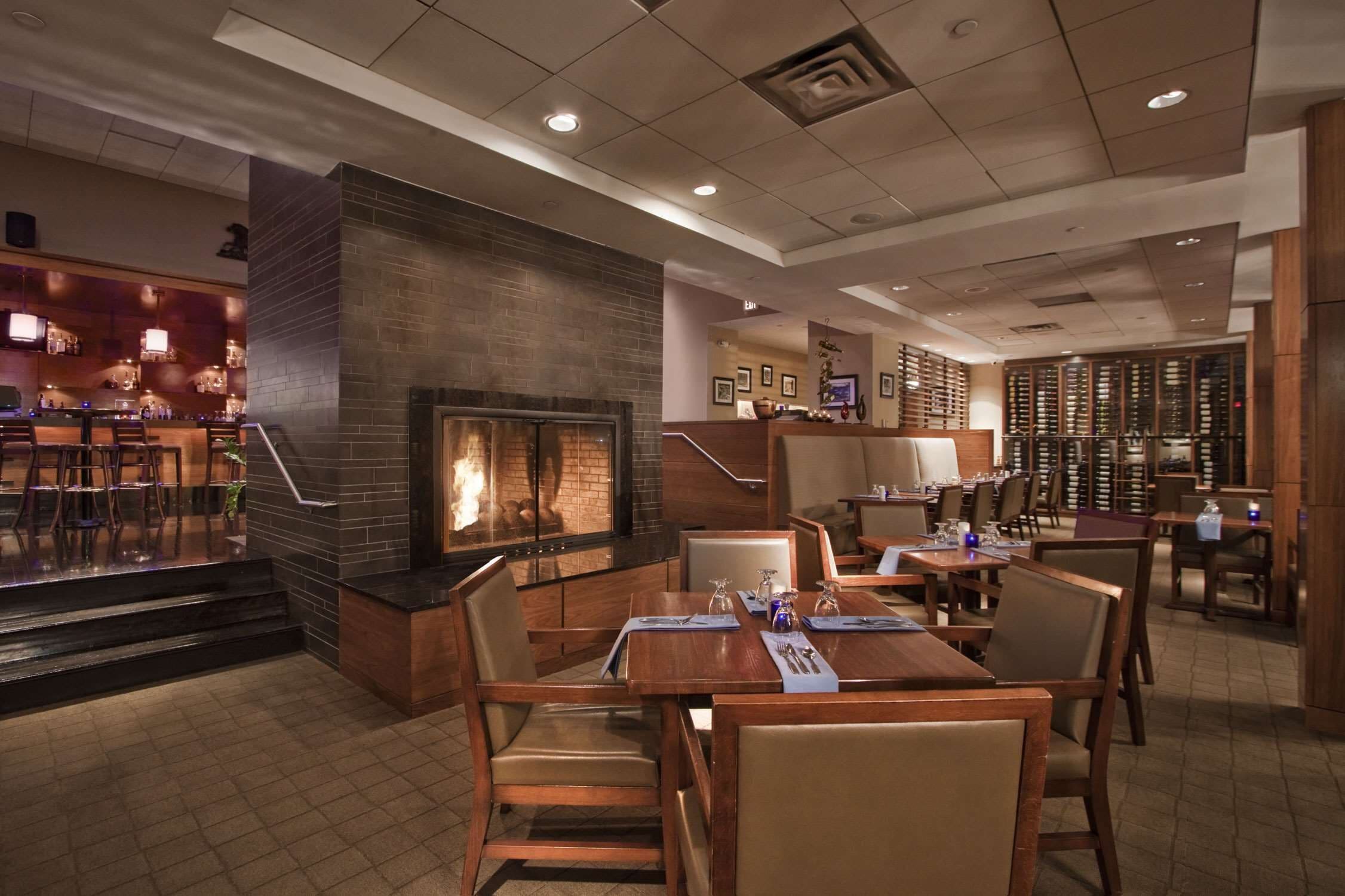 A restaurant with a brick fireplace, wooden tables, and chairs.