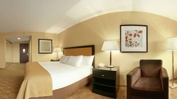 A hotel room with a bed, desk, chair, bedside table, lamp, and a view of the outdoors.