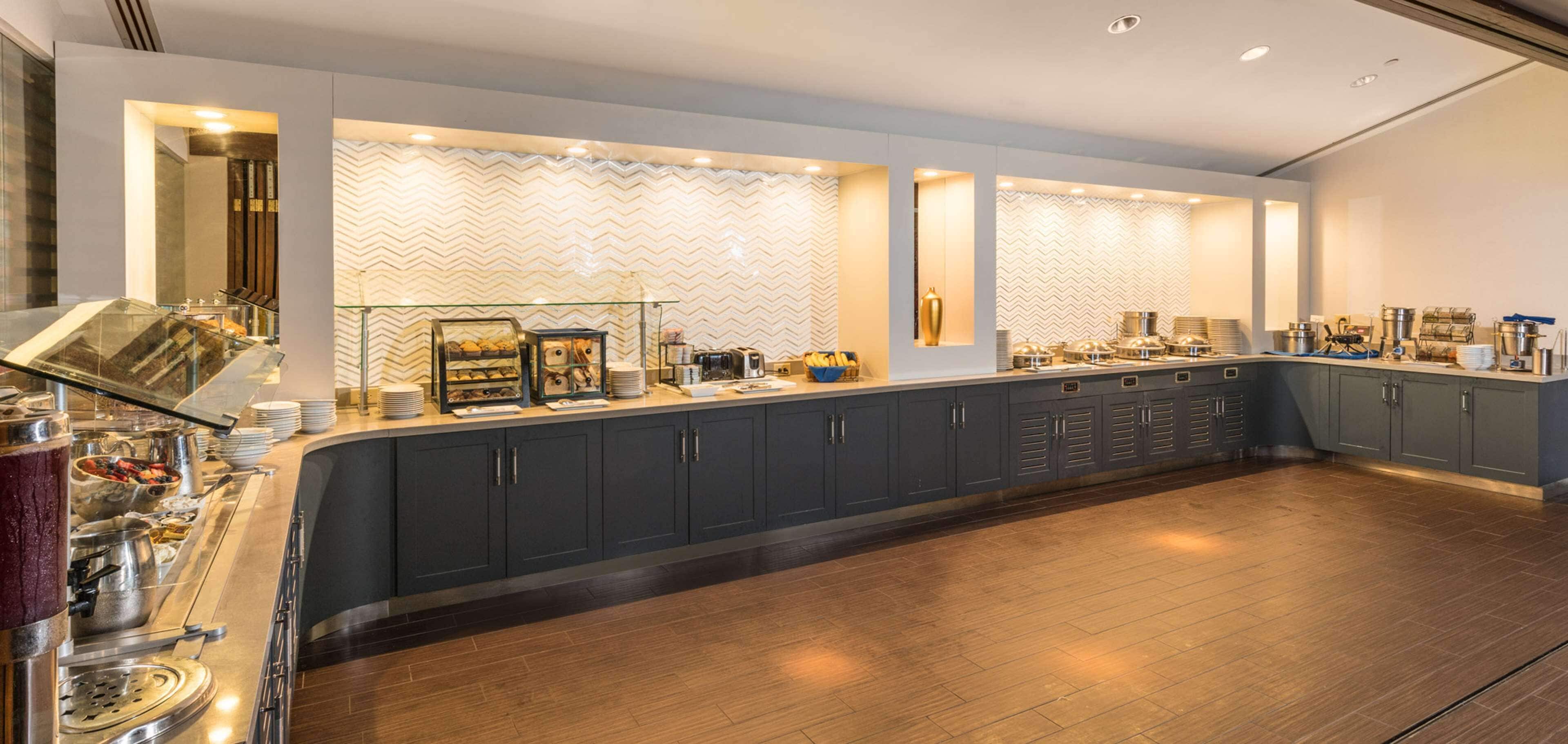 Un bar à petit-déjeuner moderne au design incurvé, doté de différents distributeurs de nourriture et de boissons, et agrémenté d’un mur à motifs en arrière-plan.