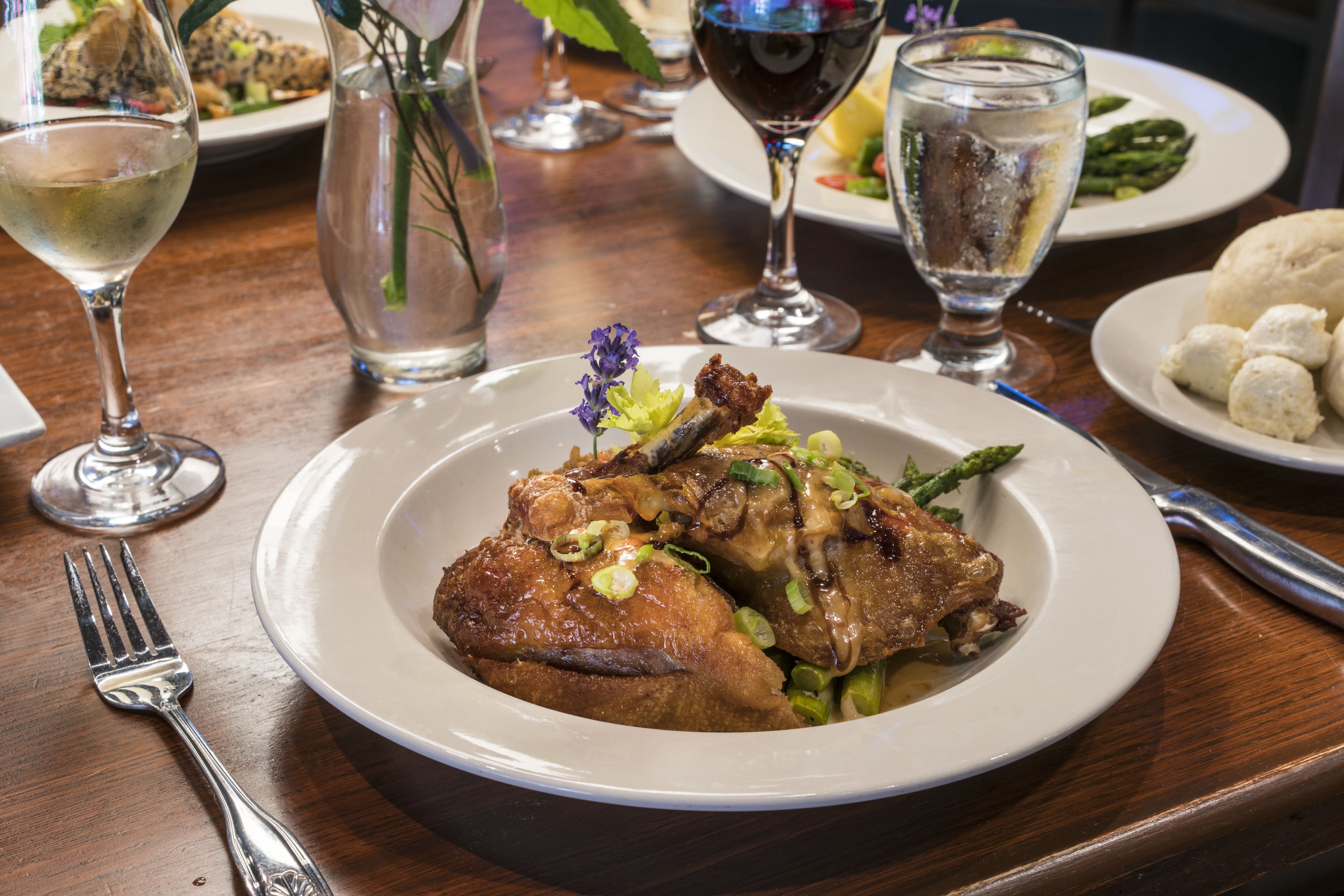 A dining table with a plate of food, a glass of wine, and a vase with flowers.