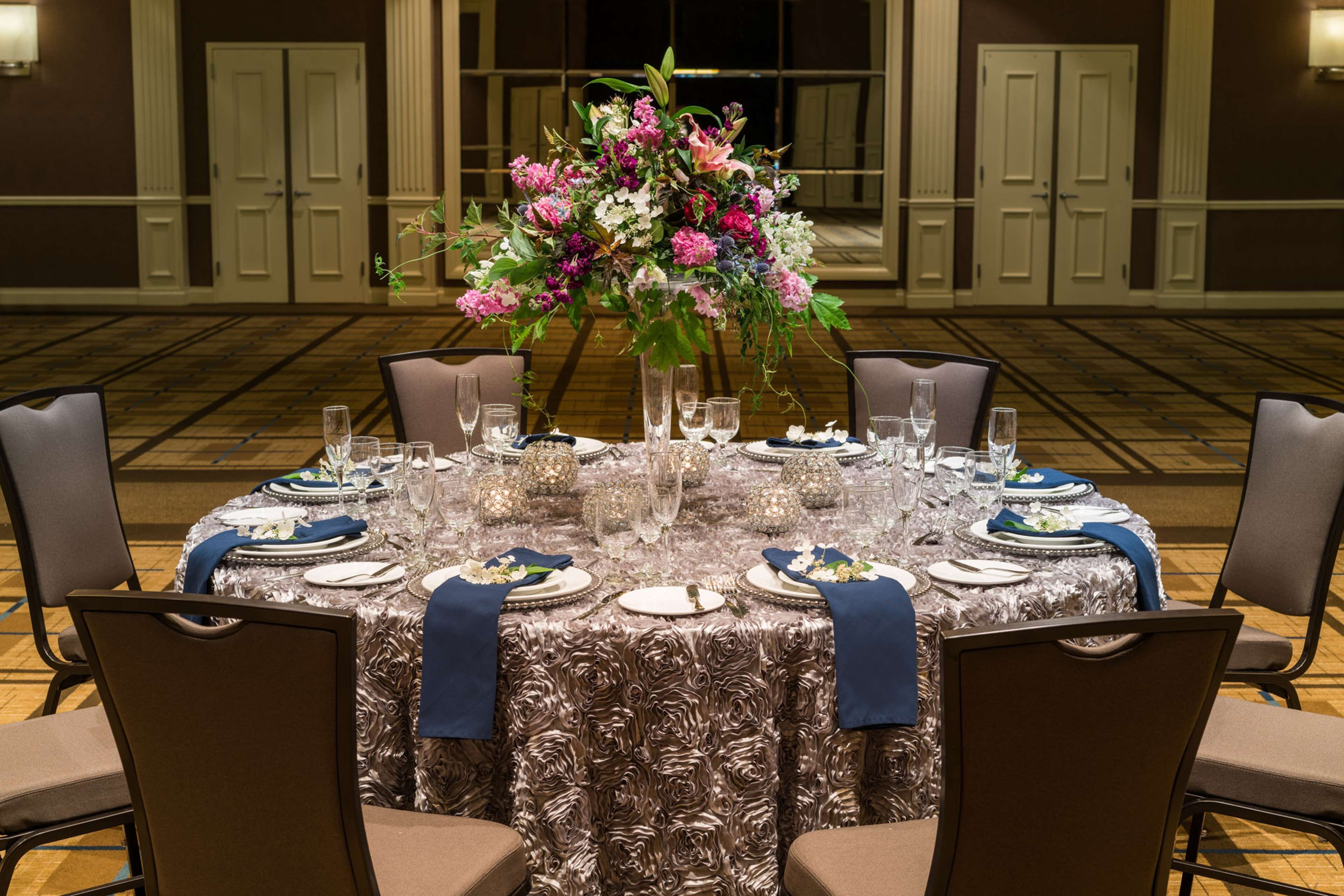 A round dining table set for eight with a floral centerpiece, surrounded by chairs.