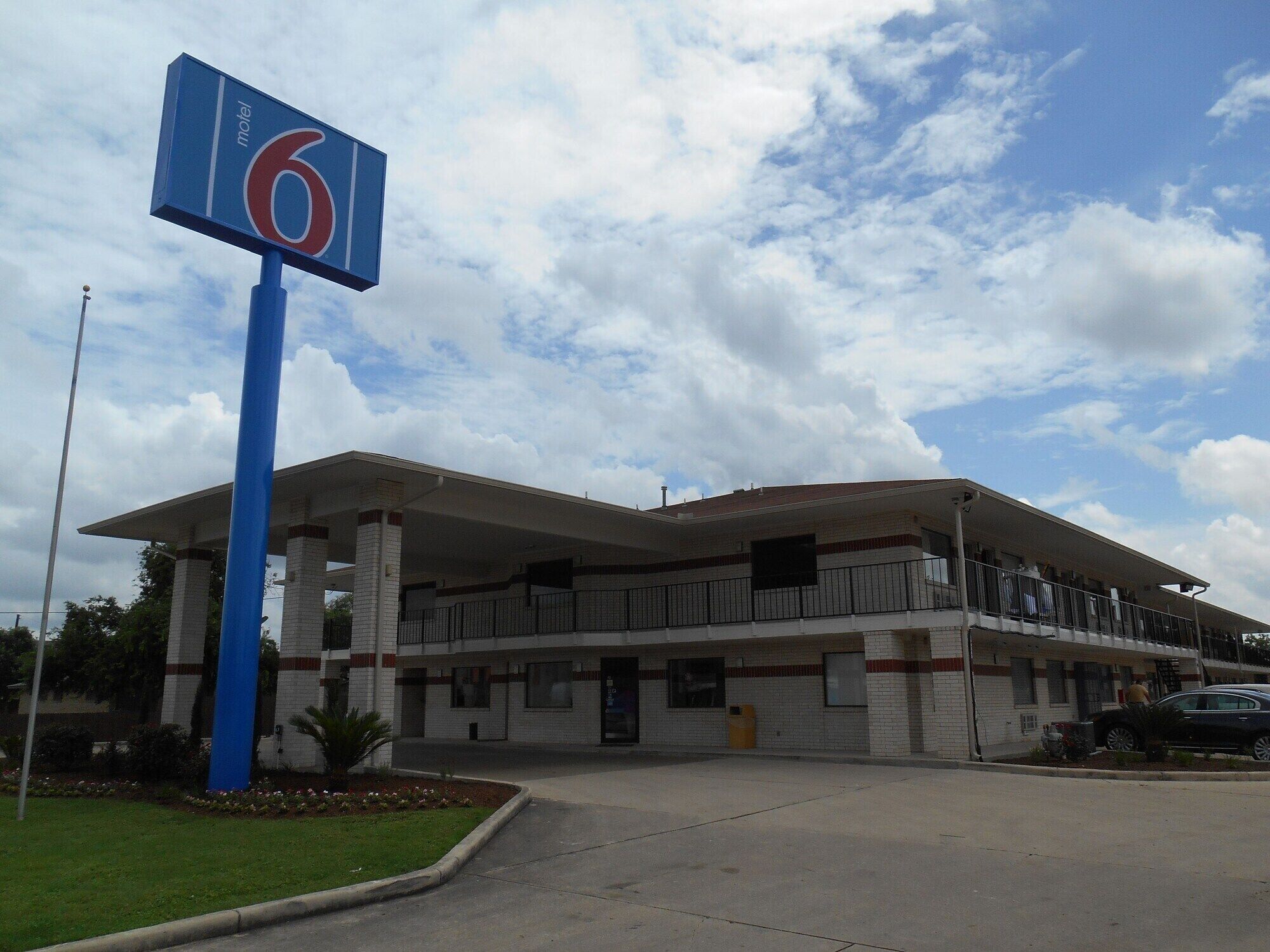 A motel with a large sign indicating it is number 6. It features a covered parking area and a two-story building with a flat roof.