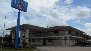 A motel with a large sign indicating it is number 6. It features a covered parking area and a two-story building with a flat roof.