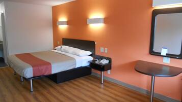 Une chambre d’hôtel avec un lit, une table de chevet et un petit bureau avec une chaise.