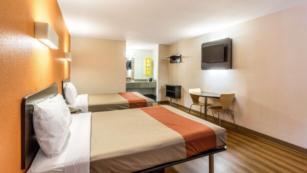 A hotel room with two beds, a desk, a chair, a television, and a bathroom visible in the background.