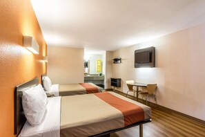 A hotel room with two beds, a desk, a chair, a television, and a bathroom visible in the background.