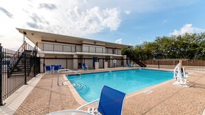 A swimming pool with lounge chairs, a covered seating area, and a building with a balcony.