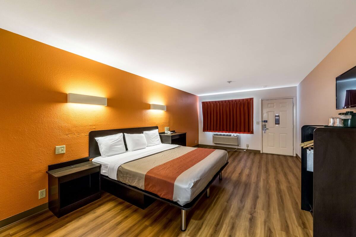 Een hotelkamer met een bed, nachtkastjes, een televisie en een raam met gordijnen.