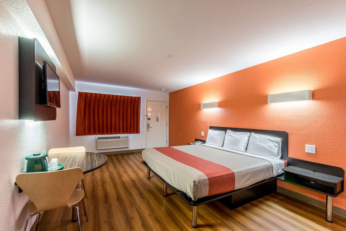 Een hotelkamer met een bed, nachtkastje, stoel en een wandtelevisie.