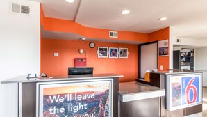 A hotel reception area with orange walls, a digital clock, and a sign that reads "We'll leave the light on for you."