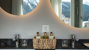 A bathroom with two sinks, a large mirror, and a view of mountains. - Hotel Steffani (St. Moritz)