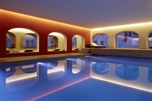 A modern indoor swimming pool with arched windows and a red wall. - Hotel Steffani (St. Moritz)