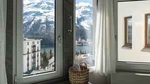 A bathroom with a bathtub, a window with a view of snow-capped mountains, and a wicker basket on the floor. - Hotel Steffani (St. Moritz)