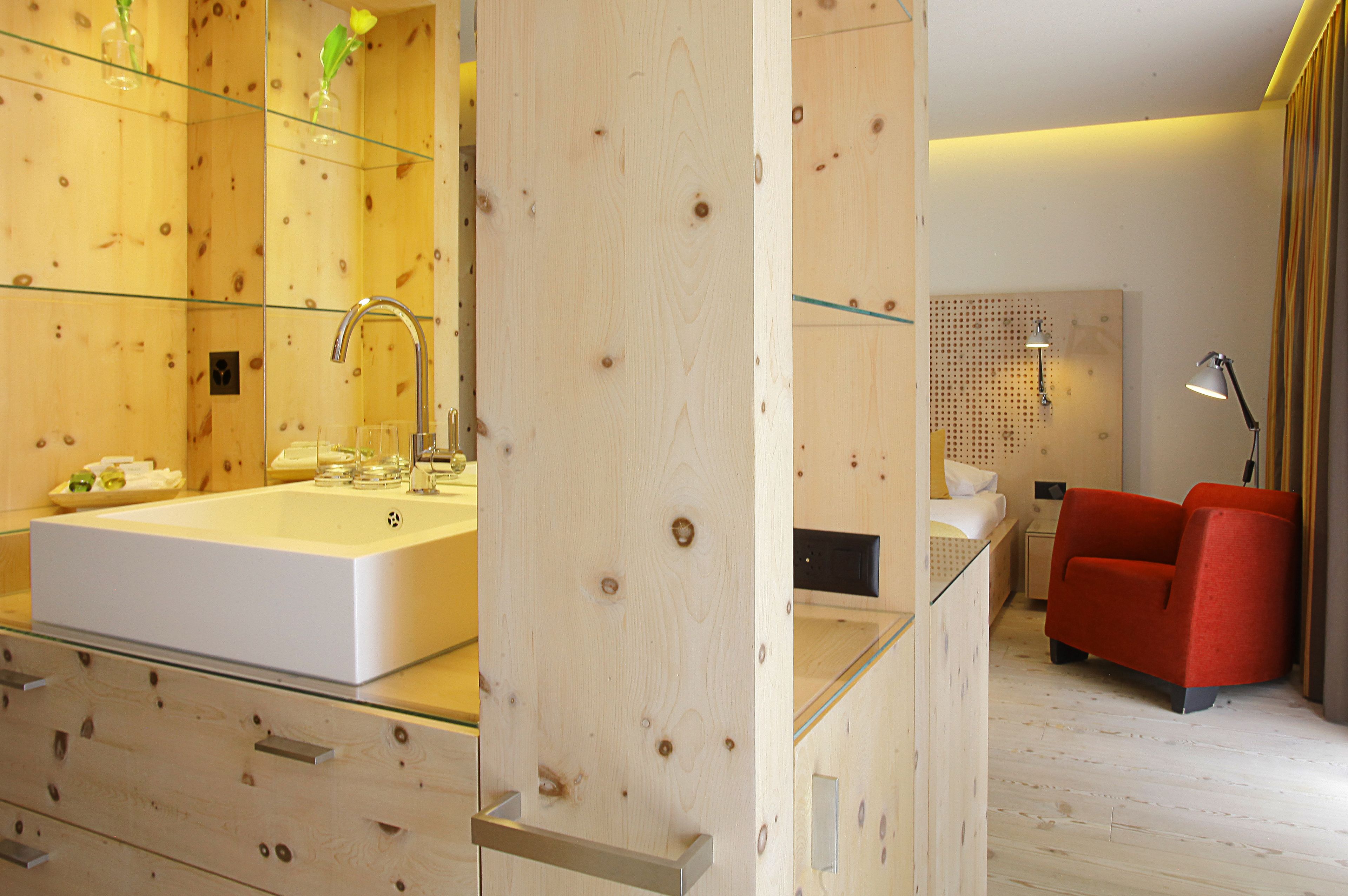 A modern bathroom with a large white sink, glass shower enclosure, and a red chair.