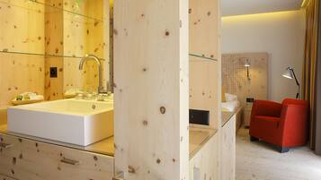 A modern bathroom with a large white sink, glass shower enclosure, and a red chair.