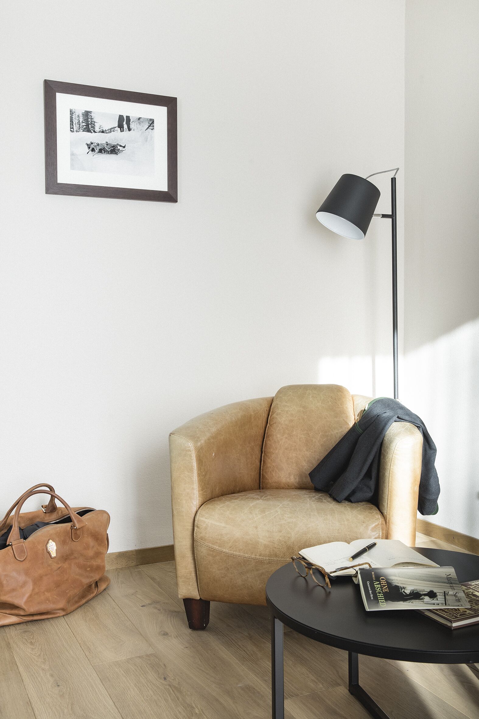 Une pièce avec un fauteuil beige, une petite table ronde sur laquelle repose un magazine, un lampadaire et un tableau encadré accroché au mur.