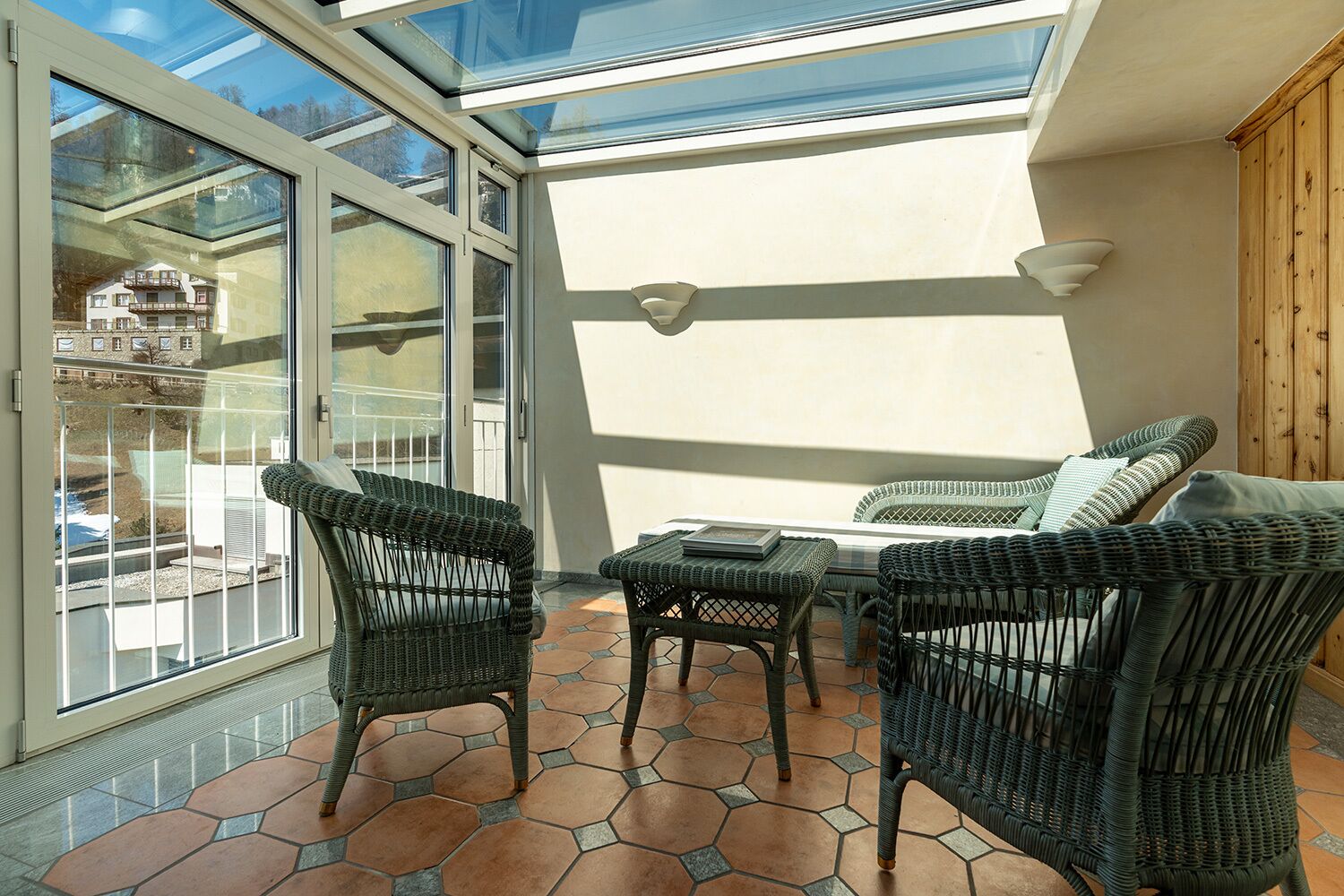 A sunlit patio with wicker furniture, a glass door leading outside, and a tiled floor.