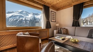 A cozy room with a sofa, a leather chair, a coffee table, and a view of snow-capped mountains. - Hotel Steffani (St. Moritz)