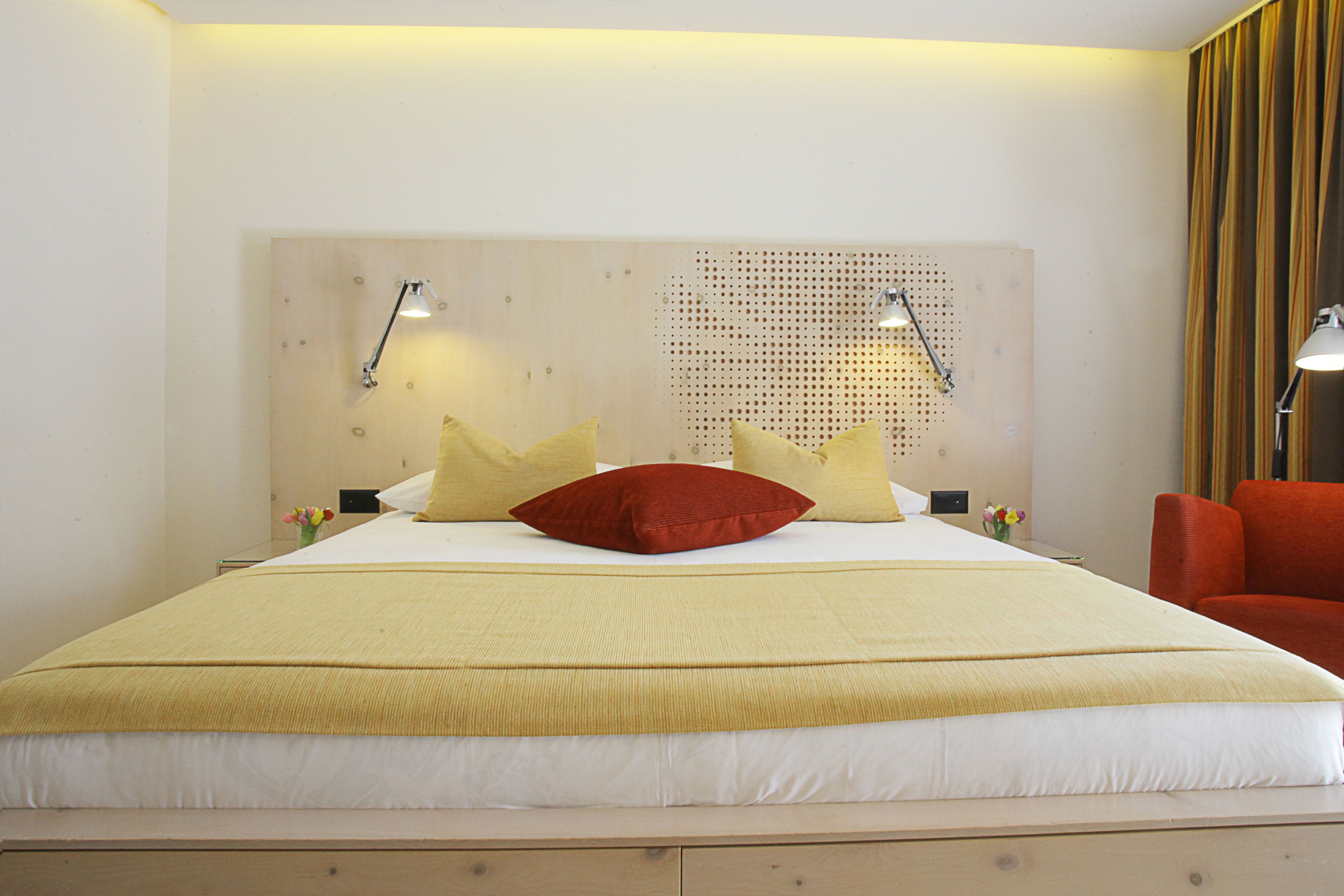 A hotel room with a large bed, a wooden headboard, two bedside lamps, and a red chair.