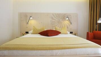 A hotel room with a large bed, a wooden headboard, two bedside lamps, and a red chair.