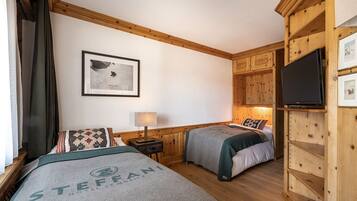 A hotel room with two beds, wooden paneling, a mounted TV, a framed picture on the wall, and a lamp on a bedside table.