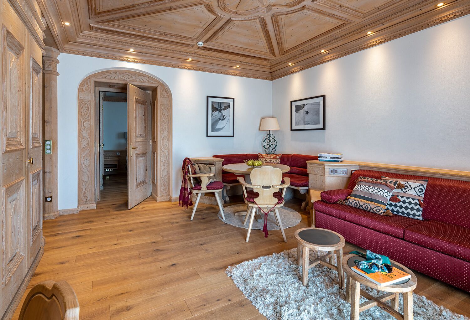 A cozy living room with a wooden floor, a red sofa, a wooden coffee table, and a small round table with a book and a pair of shoes.