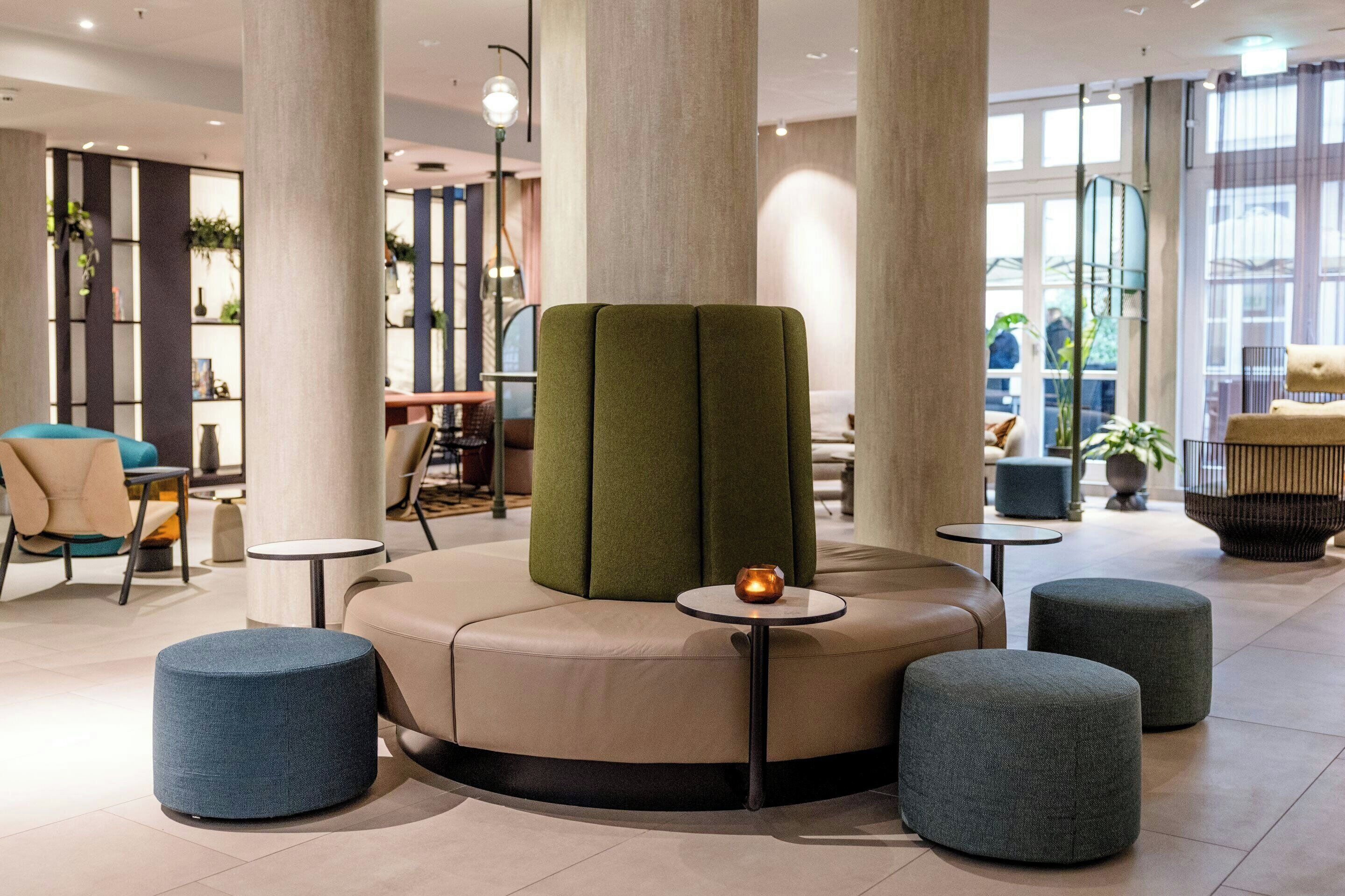 Ein moderner Lounge-Bereich mit einer runden Sitzgruppe, einem grünen Sofa in der Mitte und runden Tischen.
