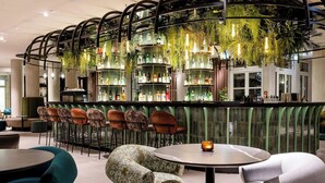 Un moderno bar con una distribución circular de asientos, barra con estantes llenos de botellas y plantas colgantes.